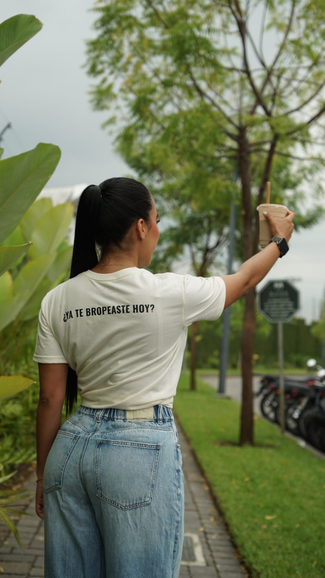 Vanessa de espaldas con la frase ¿Ya te bropeaste hoy? en la camiseta, levantando su batido
